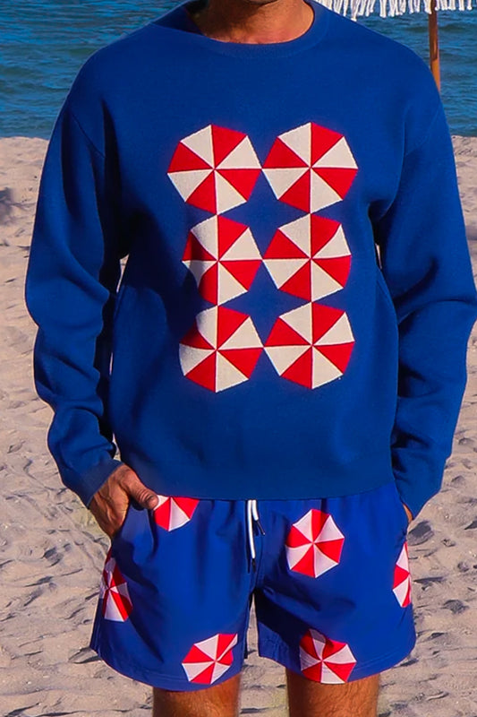 Person wearing a blue outfit with red and white geometric patterns, standing on a sandy beach.