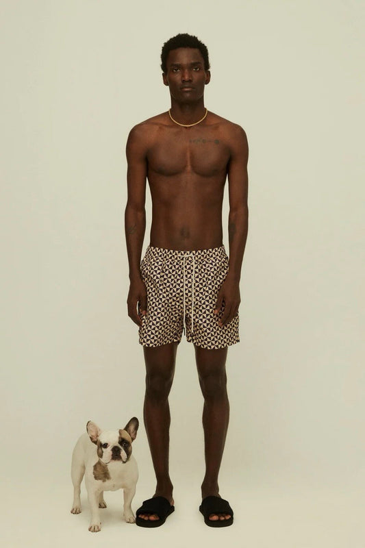 A shirtless man in patterned shorts standing next to a small dog.