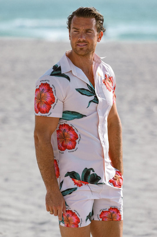 Man wearing floral shirt and shorts on the beach.